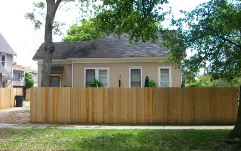 New cedar privacy fence in front of a single-storey house under shade trees, with a lawn in the foreground